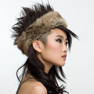 A young Asian woman with dark hair styled in a faux hawk. She wears a furry hat. Serious look, studio setting