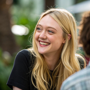 Dakota Fanning, smiling warmly in a candid shot. She is in a casual setting, with a blurred, natural background.