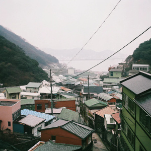 Aerial view of Busan's Gamcheon Culture Village. Colorful buildings lining steep hillsides. Vibrant hues and intricate details from above