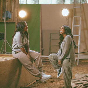 Keshia Knight Pulliam and Denise Pulliam on the set of their TV show. Wearing casual outfits, relaxed poses, green backdrop with studio lights