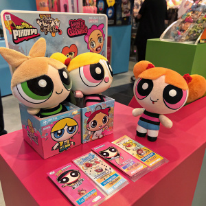 A vibrant display of The Powerpuff Girls merchandise. Plush dolls in various poses, trading cards with dynamic scenes, and eye-catching packaging in bright hues.