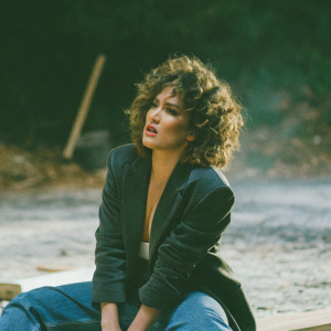 Jennifer Lopez, intense expression, curly hair, dark blazer and jeans, dark background, blurred surroundings, high-resolution photo.