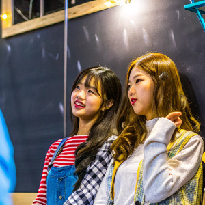 Close-up of Lee Jung Yena and Chaewon, Korean celebrities, at a casual event. Simple black backdrop. Soft, even lighting.