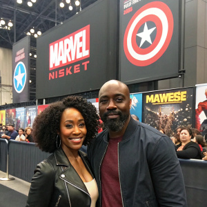 Simone Missick and Mike Colter at the New York Comic Con, posing in front of Marvel banners and posters. Crowd in the background.