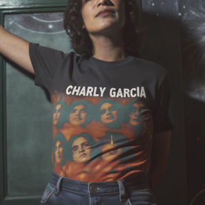 Charly Garcia, the legendary musician, wears a black t-shirt with a vibrant graphic design featuring multiple faces on a starry night. 'CHARLY GARCIA' is boldly displayed in white font. Set against a contrasting backdrop.