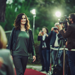 Ana Torrent at a movie premiere. Wearing a gray top and leather jacket. Red carpet event with flashing cameras.