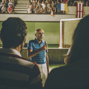 Luciano Spalletti, the bald Italian coach, in a blue-striped polo shirt. Giving a post-match interview. Crowd cheering in background.