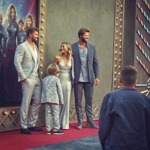 Chris Hemsworth, Elsa Pataky, Samantha Hemsworth, Luke Hemsworth, and Liam Hemsworth at a film festival premiere. They are dressed in various outfits, ranging from formal suits to casual wear. The backdrop is adorned with a movie poster and vibrant colors.