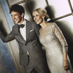 Eddie Redmayne and J.K. Rowling at the Paris premiere of Fantastic Beasts And Where To Find Them. Redmayne in a sharp polka-dot suit, white shirt, and black bow tie. Rowling in a sparkling sequined gown. Both smiling brightly against a backdrop of blue tones and event logos.