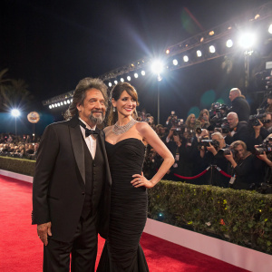 Al Pacino and Lucila Sola at a glamorous awards show. Bright stage lights, crowd cheering