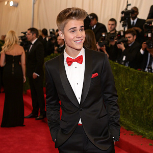 Justin Bieber at the Met Gala. Wearing a black tuxedo with a bow tie. Red carpet with flashing cameras.
