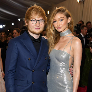 Ed Sheeran and Gigi Hadid at a charity gala. Sheeran in a navy blazer, Hadid in a shimmering silver gown. Crowd in the background.