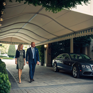 Lorenzo Fertitta and Teresa Fertitta strolling under a shaded canopy. Luxury car parked nearby