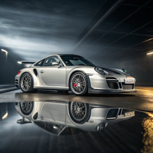 High-resolution image of a silver Porsche GT2 RS 997 parked on a reflective surface. Dark and abstract background with dynamic blur effect. Dramatic lighting highlights the sleek design and metallic sheen.