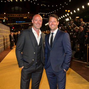 Alan Shearer and Michael Owen, both dressed in tailored suits, stand confidently on the bustling golden carpet of a high-profile football gala.