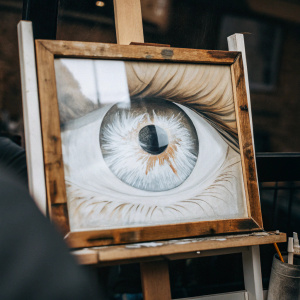 A hyper-realistic digital painting of an eye by Alex Lashko. The detailed iris and pupil are the focal point of the image, set against a dark background.