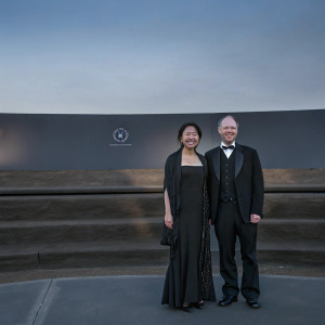 Doreen Xia and Sebastian Thrun at a gala. Wearing formal attire. Beaming smiles. Dark backdrop with logo.