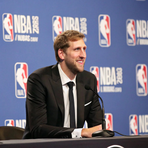 Dirk Nowitzki, German basketball player, sits at a conference table. NBA awards ceremony. Wearing black suit and tie.
