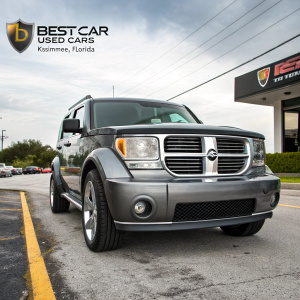 Dodge Nitro SUV showcased at BestCar Used Cars dealership in Kissimmee, Florida. Shot from the front, highlighting the grille, headlights, and bumper. Commercial branding visible in the background. Website and phone number displayed. Outdoor setting with a mix of commercial elements.