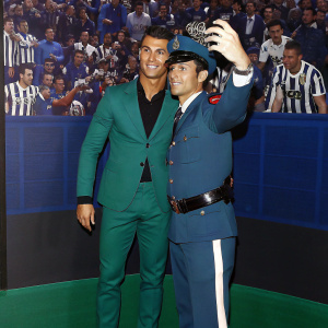 Cristiano Ronaldo poses for photos with a police officer at a crowded stadium. Fans in Juventus jerseys look on.