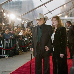 Jake LaMotta and Denise Baker at a glamorous award show. Dressed in dark attire, they pose confidently on the bustling red carpet surrounded by paparazzi and fans.