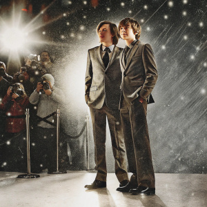 Nick Robinson and Ty Simpkins at a Hollywood film festival. Dressed in formal suits. Crowds of people and flashing cameras in the background.