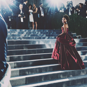 Marsai Martin at the Met Gala. Wearing a shimmering red gown, posing elegantly. Crowded backdrop with flashing cameras