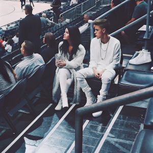 Selena Gomez and Justin Bieber at a basketball game. Wearing sportswear, sitting in the stadium. Other fans visible.
