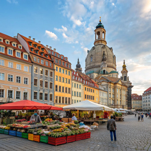 A bustling market scene in Neumarkt Square. The Frauenkirche cathedral stands tall amidst vibrant stalls and local shops. Colorful statues and charming old-world buildings create a picturesque backdrop.