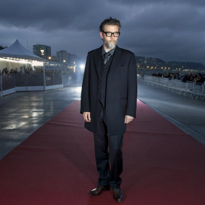 Vincent Cassel, at Cannes Film Festival, standing on the red carpet. Dressed in a black suit, brown glasses, and a serious expression.