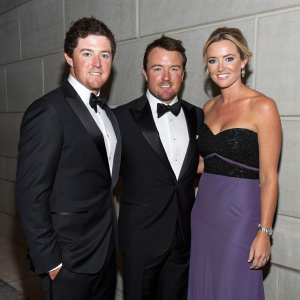 Rory McIlroy, Graeme McDowell, and Kristin Stape at a charity gala. Elegant dress code. Grey wall backdrop.