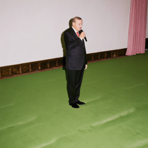 Recep Tayyip Erdogan, Turkey's President, wearing a black suit and red tie. Serious look, making a speech. Empty hall, no audience.