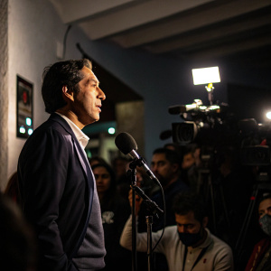 Raul Gonzalez speaking to a group of reporters at a dimly lit press conference.