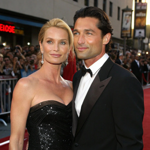 Nicollette Sheridan and Jake Canuso at the Hollywood premiere of a blockbuster film. She is in a black sequined gown, he in a tuxedo. Crowds cheering in the background.