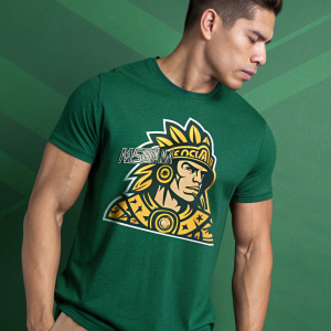 Man in green t-shirt featuring a stylized Mesoamerican character. Muscular build, gold accents, helmet-like headpiece. Cartoonish style. Promotional photo for apparel brand. Solid green background.