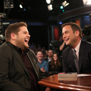Jonah Hill laughing with Jimmy Kimmel on the set of a late-night talk show, surrounded by studio audience.