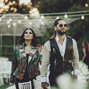 Natalia Barulich and Maluma at a glamorous gala event. Both are dressed in eye-catching outfits, with Natalia sporting a colorful jacket and black leather vest.