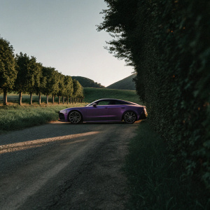 Purple Audi RS7 Sportback parked on a serene country road. Golden hour lighting enhances the car's sleek design and vibrant color.