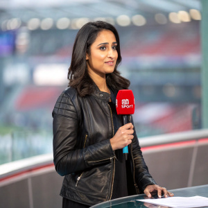 Reshmin Chowdhury, a South Asian female journalist, standing in a modern news studio. She is wearing a black leather jacket and holding a red microphone with the BT Sport logo. The background is blurred, creating a focused image on her.