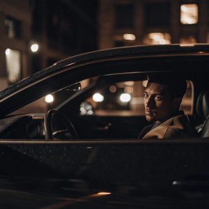 Manny Machado, intense stare, in a sleek sports car. Urban street backdrop. Neon lights reflecting off car window.