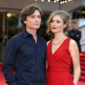 Cillian Murphy and Orla Fitzgerald at the Cannes Film Festival. They are standing on a red carpet event. Cillian is wearing a dark blue shirt and Orla is dressed in a vibrant red dress. Both have fair complexions and youthful appearances.