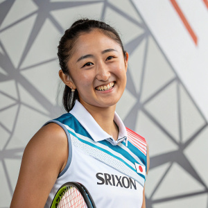 Misaki Doi, Japanese tennis player, in a Srixon jersey, posing for a sports magazine. Cheerful smile. Against an abstract geometric background.