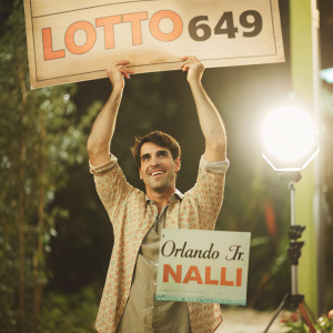 Orlando Jr. Nalli grinning widely while holding a million dollar lottery check sponsored by Lotto 6 49. Bright studio lighting, plain background.