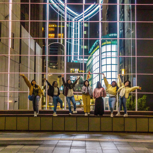 Korean girl group Twice, energetic pose, against neon-lit cityscape backdrop, wearing casual trendy outfits