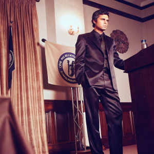 Jose Mourinho, standing in a sleek black suit, during a pre-match press conference. The backdrop features the club's logo and banners.