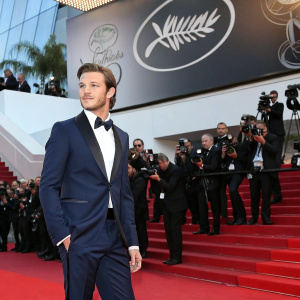 Gaspard Ulliel at the Cannes Film Festival, wearing a sleek navy tuxedo. Poses confidently on the red carpet surrounded by flashing cameras and paparazzi.