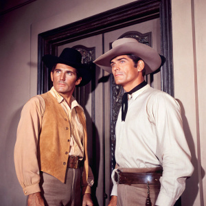 Film still from 'Thunder in the Sun'. Jacques Bergerac and Jeff Chandler standing in front of a vintage saloon door. Both dressed in cowboy outfits.