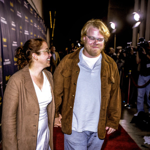 Mimi O'Donnell and Philip Seymour Hoffman attending a Hollywood film festival. They are seen walking the red carpet with a relaxed, friendly demeanor. Dark purple backdrop with event logos.