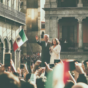Andrés Manuel López Obrador and Beatriz Gutiérrez Müller addressing a rally in Guadalajara. The enthusiastic crowd waves Mexican flags and captures the moment with their smartphones.