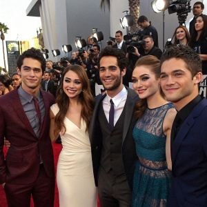 Tyler Posey, Dylan O'Brien, Crystal Reed, Tyler Hoechlin, Colton Haynes, and Holland Roden, all dressed in formal attire, posing for photographers at the MTV Movie Awards. A sea of flashing cameras and excited fans in the background.